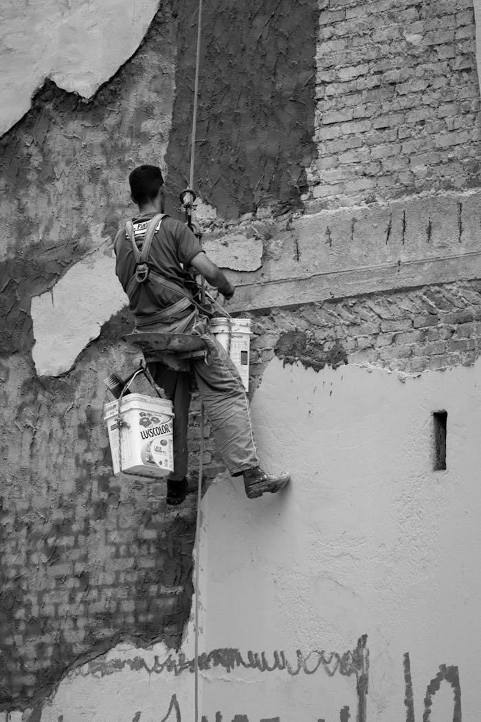 Black and white photo of a worker on a rope restoring a wall.