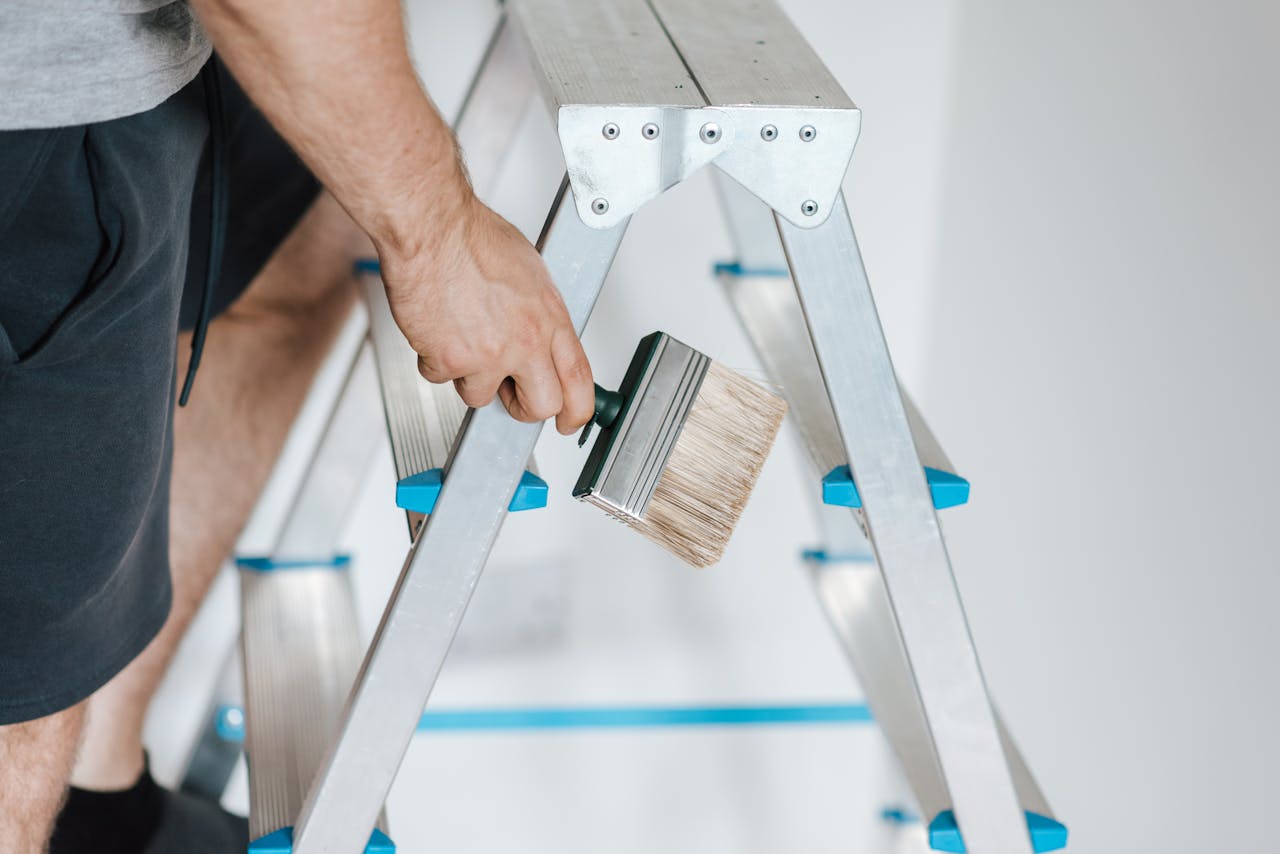 Close-up of a painter on a ladder holding a wide brush, ready for home renovation.