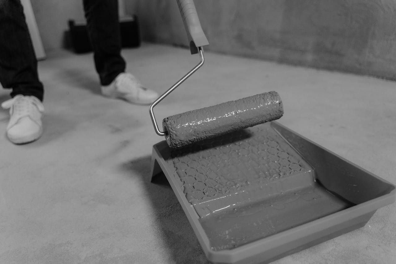 Black and white close-up of a paint roller and tray during a home renovation.